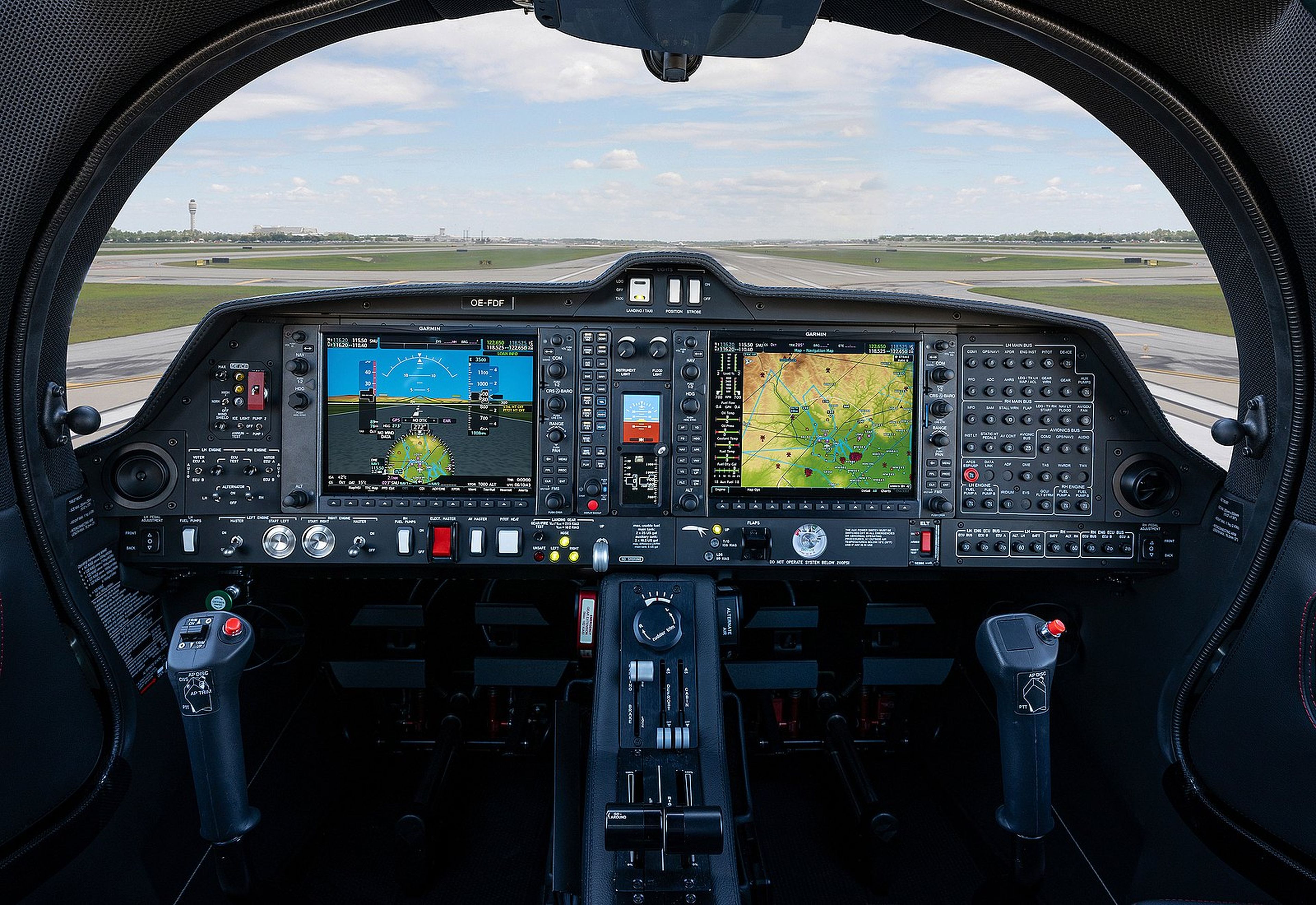 Cockpit view of a modern aircraft featuring digital displays, control panels, and a runway visible through the windshield.