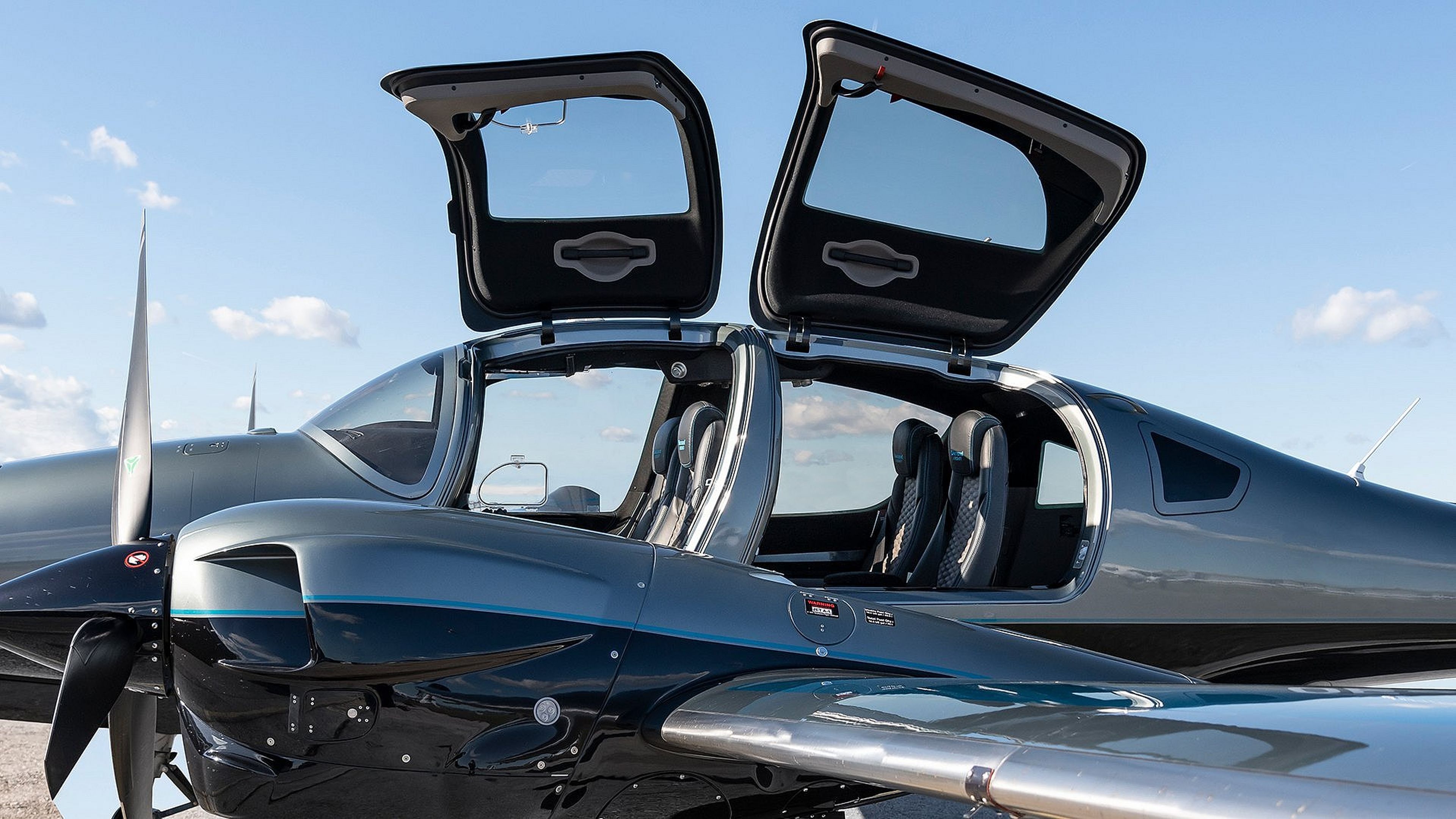 A sleek, modern light aircraft with open gull-wing doors, revealing its interior seating, under a clear blue sky.
