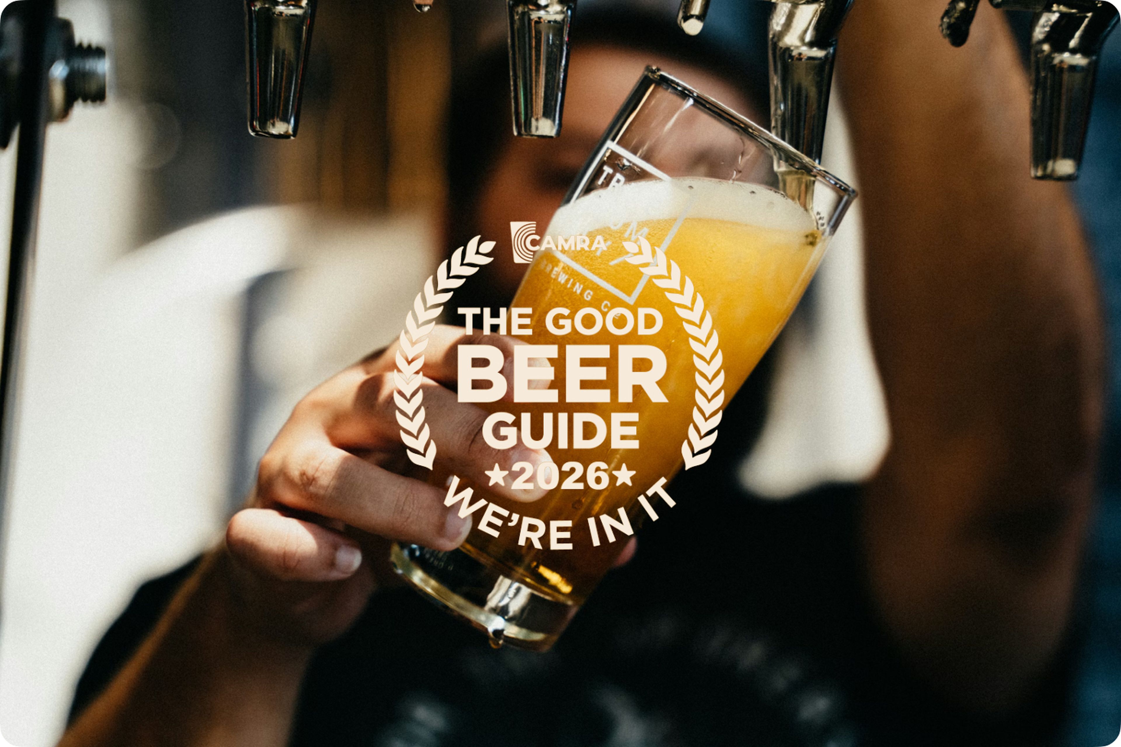 A person fills a glass with beer from a tap. The glass displays "CAMRA, The Good Beer Guide 2026, We're In It" in bold text.