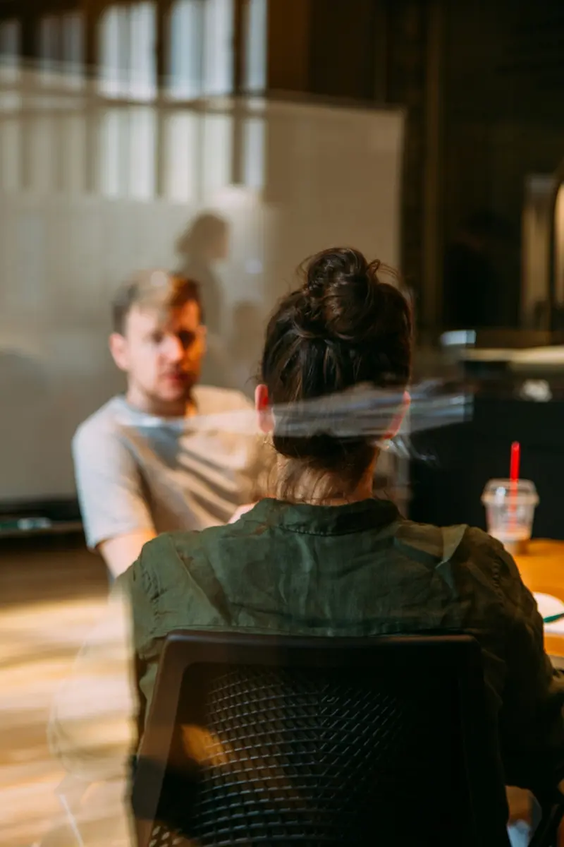 Two colleagues in conversation across a table, seen through glass in warm light