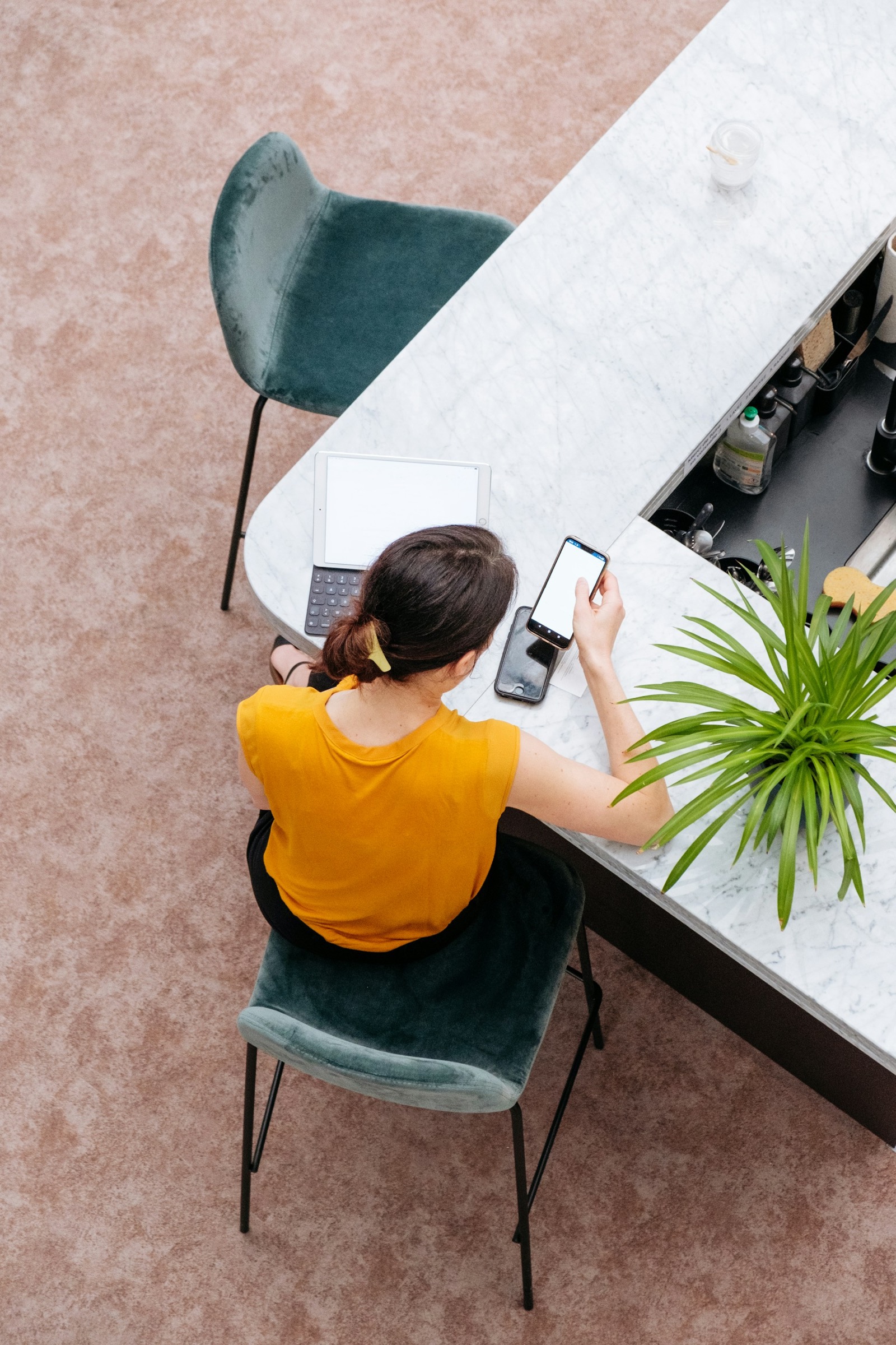 A person working across a tablet and a phone at a marble counter, seen from above