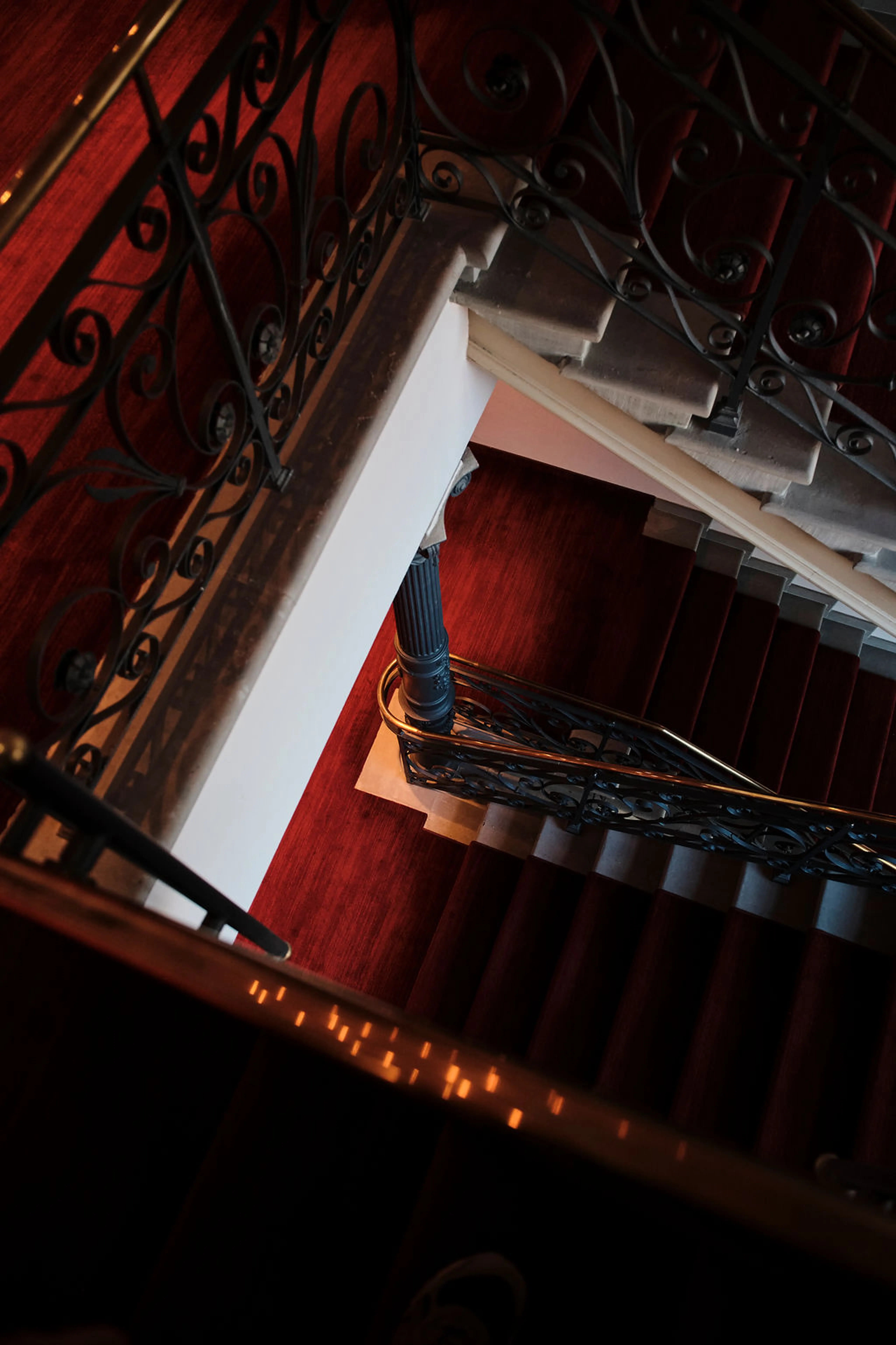 Blick von oben auf eine Wendeltreppe mit rotem Teppich und kunstvollen Schmiedeeisengeländern.