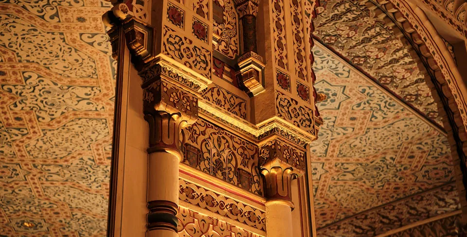 Verzierte Architektur mit goldenen Säulen und detailliert gemusterten Decken in warmem Licht.