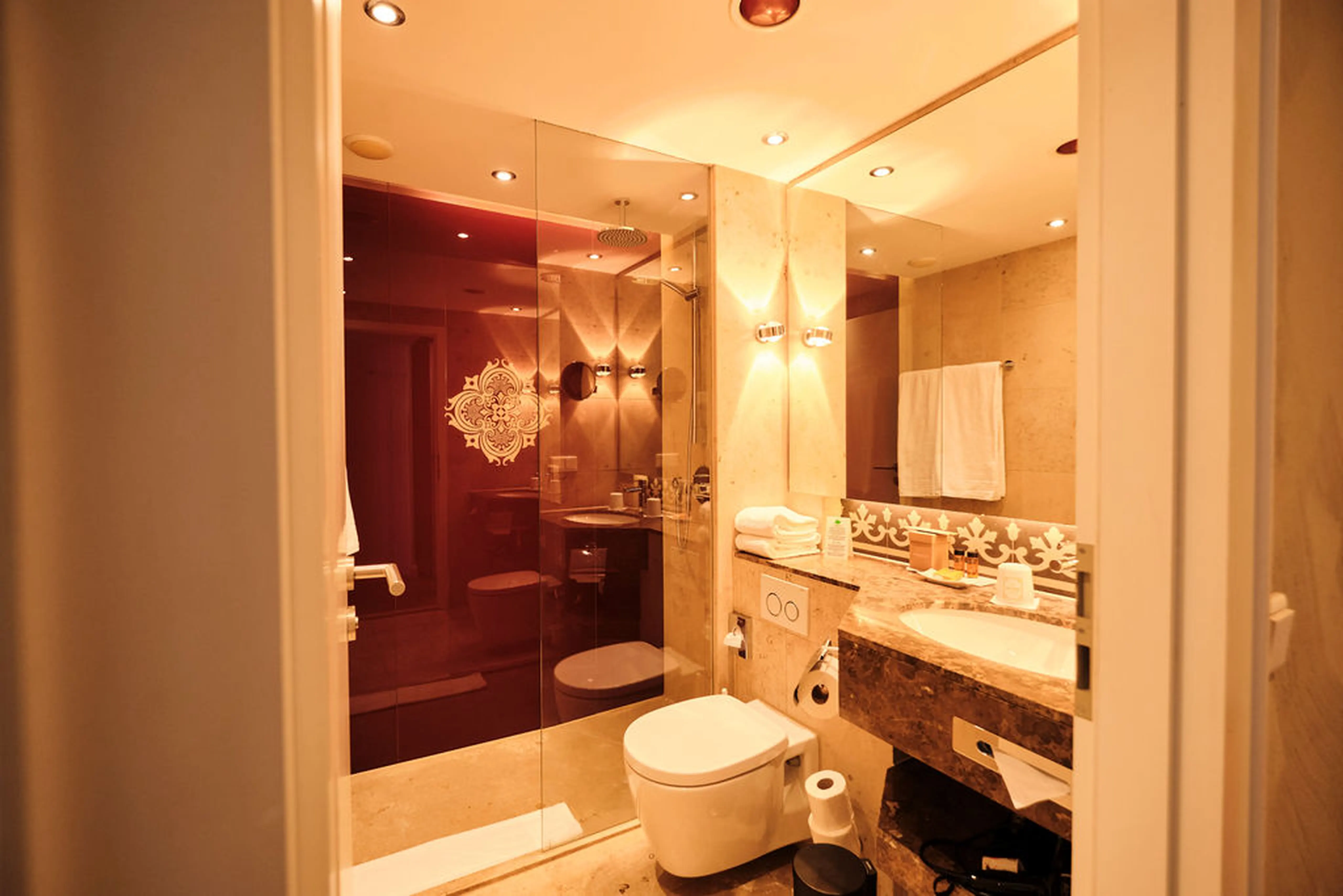 Modernes Badezimmer mit Glasdusche, WC und Waschbecken, dekoriert mit Handtüchern und warmem Licht.