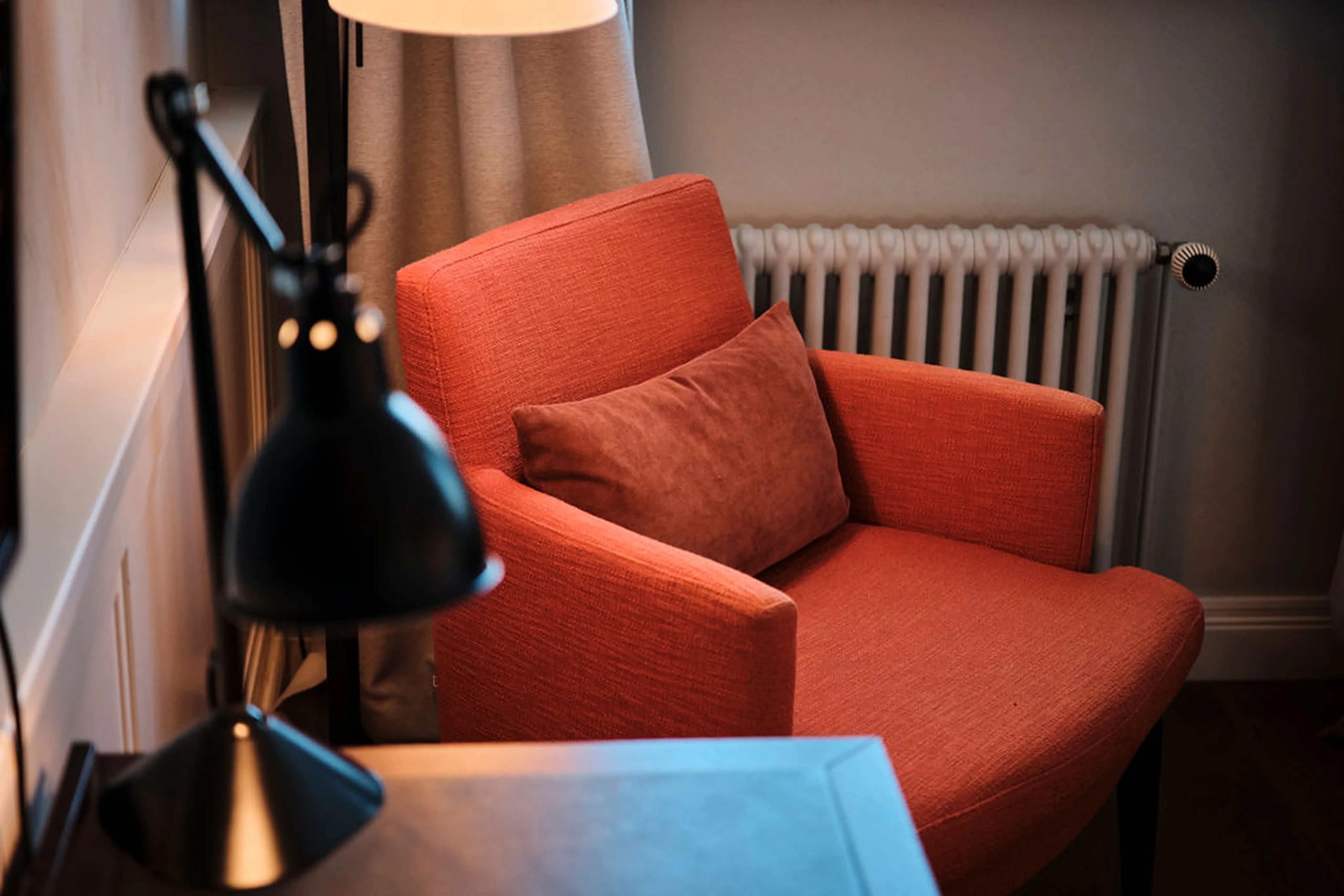 Roter Sessel mit Kissen neben einer Lampe und einem Heizkörper in einem gemütlichen Raum.