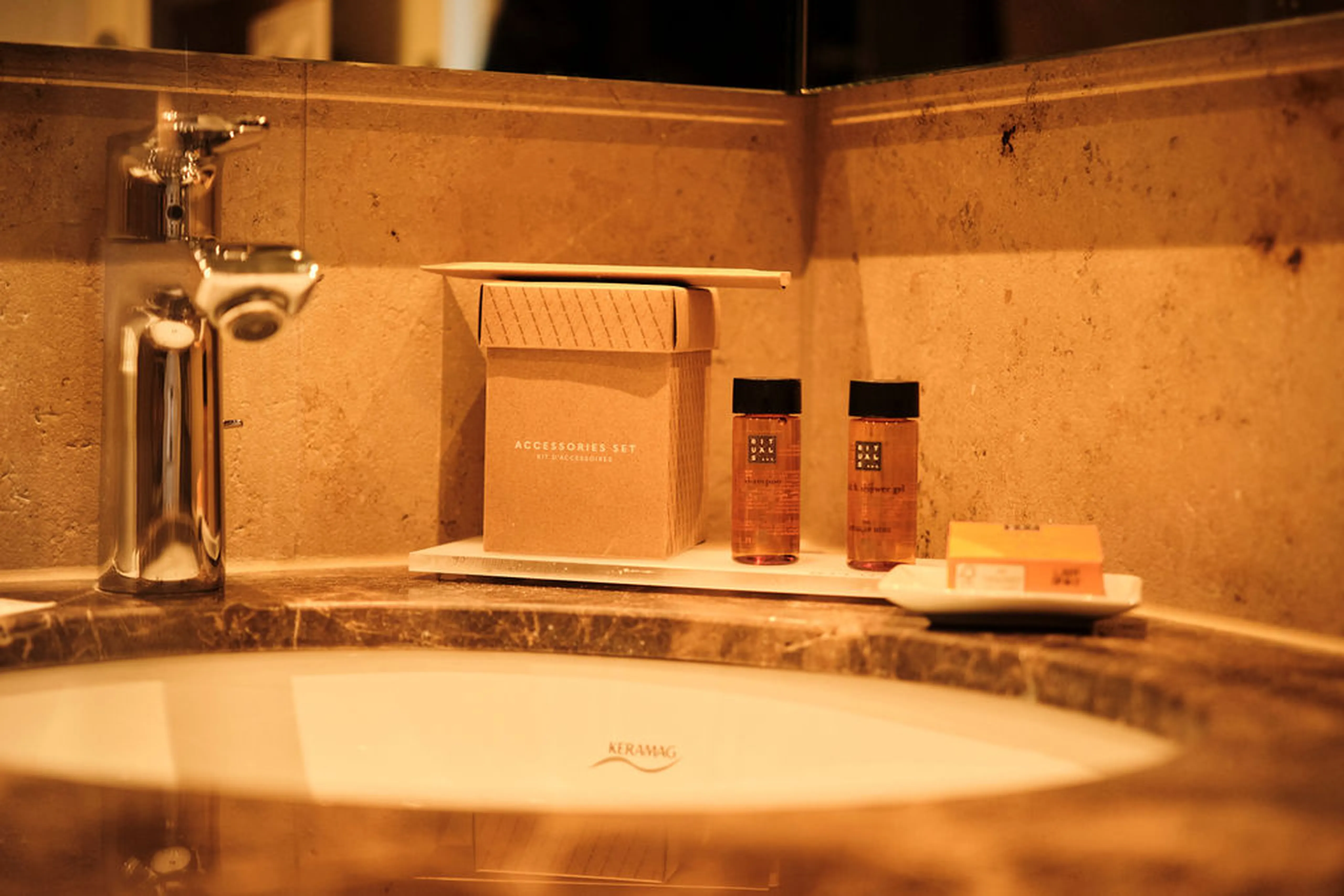 Waschbecken mit Seifenspender, Accessoire-Set-Schachtel und Rituals-Duschgelflaschen auf einem Tablett in einem elegant eingerichteten Badezimmer.