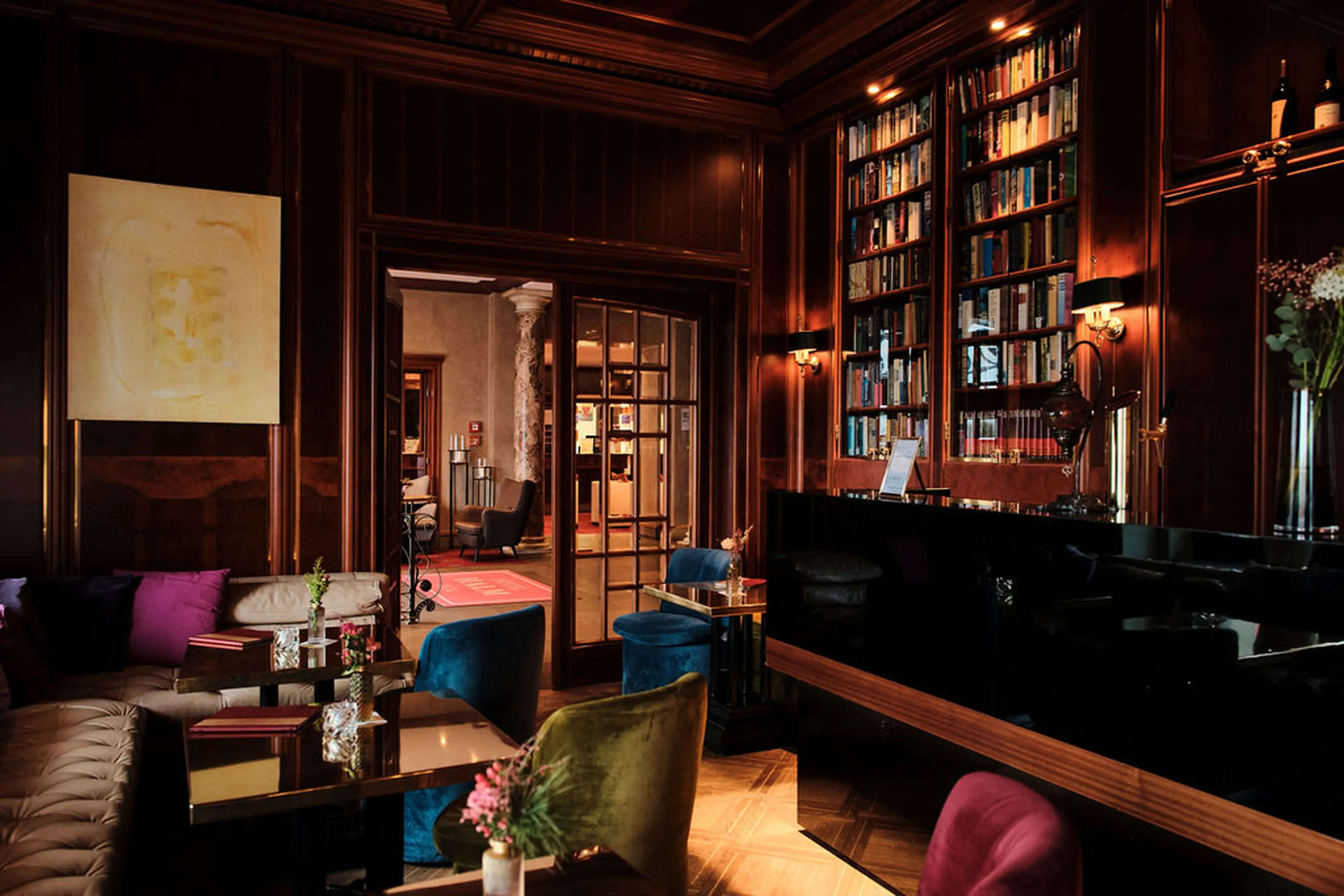 Elegante Bibliothek mit dunklen Holzwänden, Bücherregalen, bequemen Sesseln, einem einladenden Sofa und gedämpfter Beleuchtung.