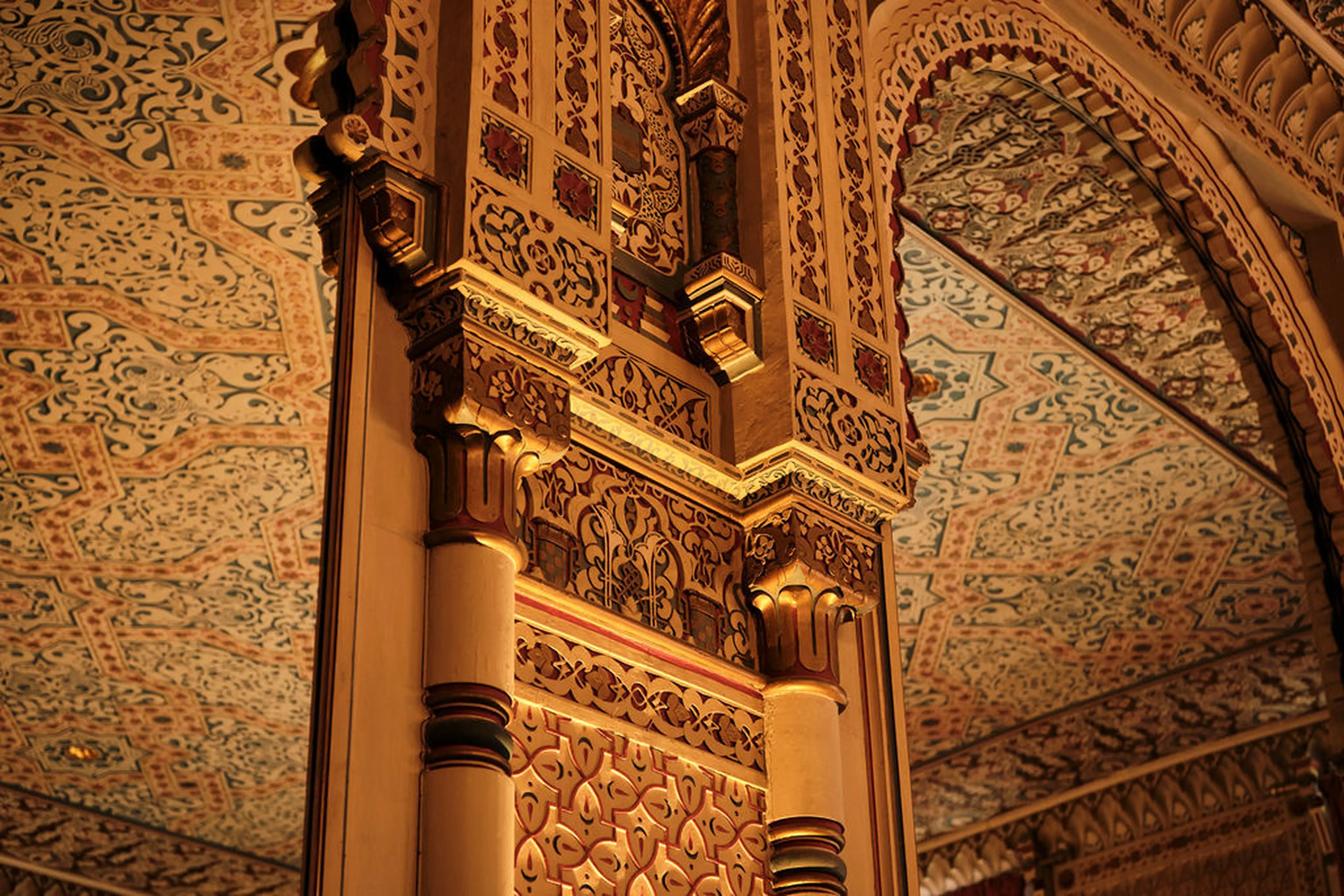 Detailreiche, goldverzierte Säulen und kunstvoll verzierte Decken in einem historischen Gebäude. Dekorative, orientalische Muster.