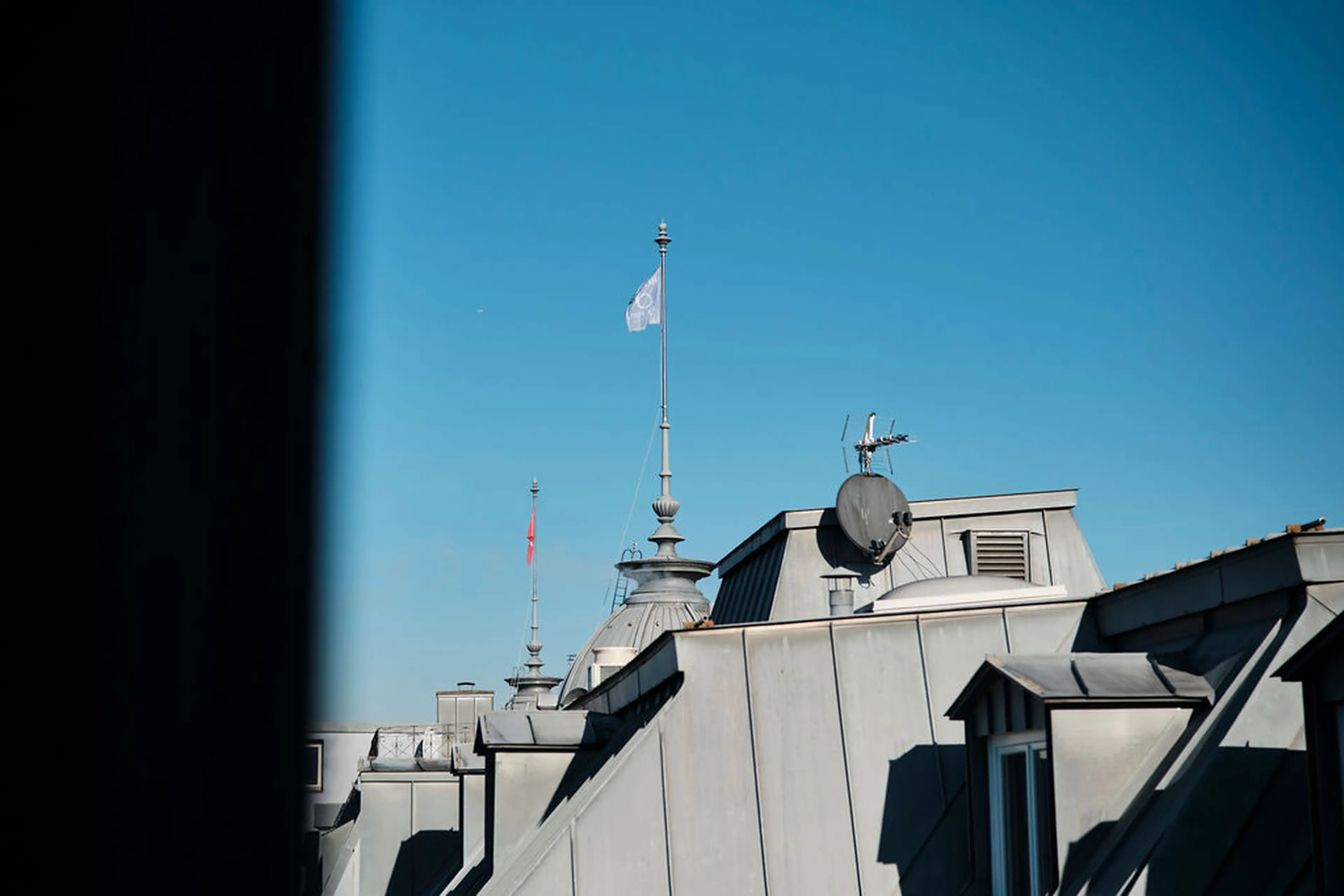 Blick auf mehrere Dächer mit Antennen und Fahnenmast bei klarem blauen Himmel.