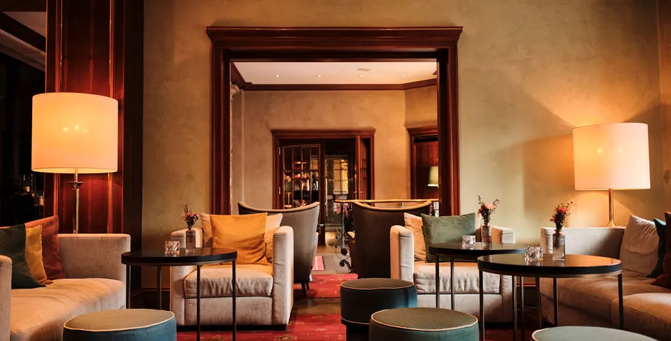 Gemütliche Hotellounge mit Sofas, runden Tischen und Lampen. Der Raum hat warme Beleuchtung und elegante Holzakzente.