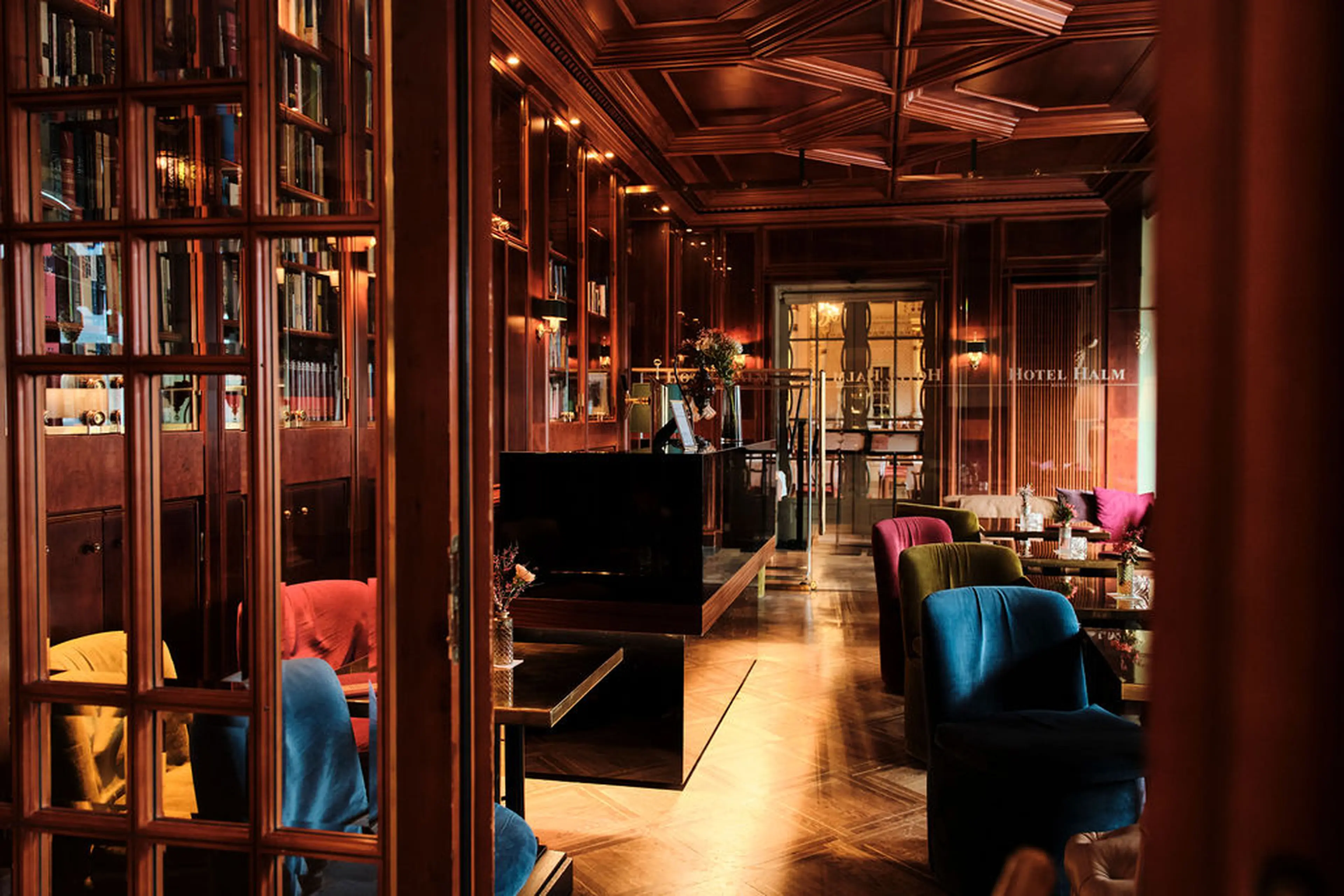 Elegante Hotel-Lounge mit Holzvertäfelung, bunten Sesseln und Bücherregalen. Gedämpftes Licht schafft eine gemütliche Atmosphäre.