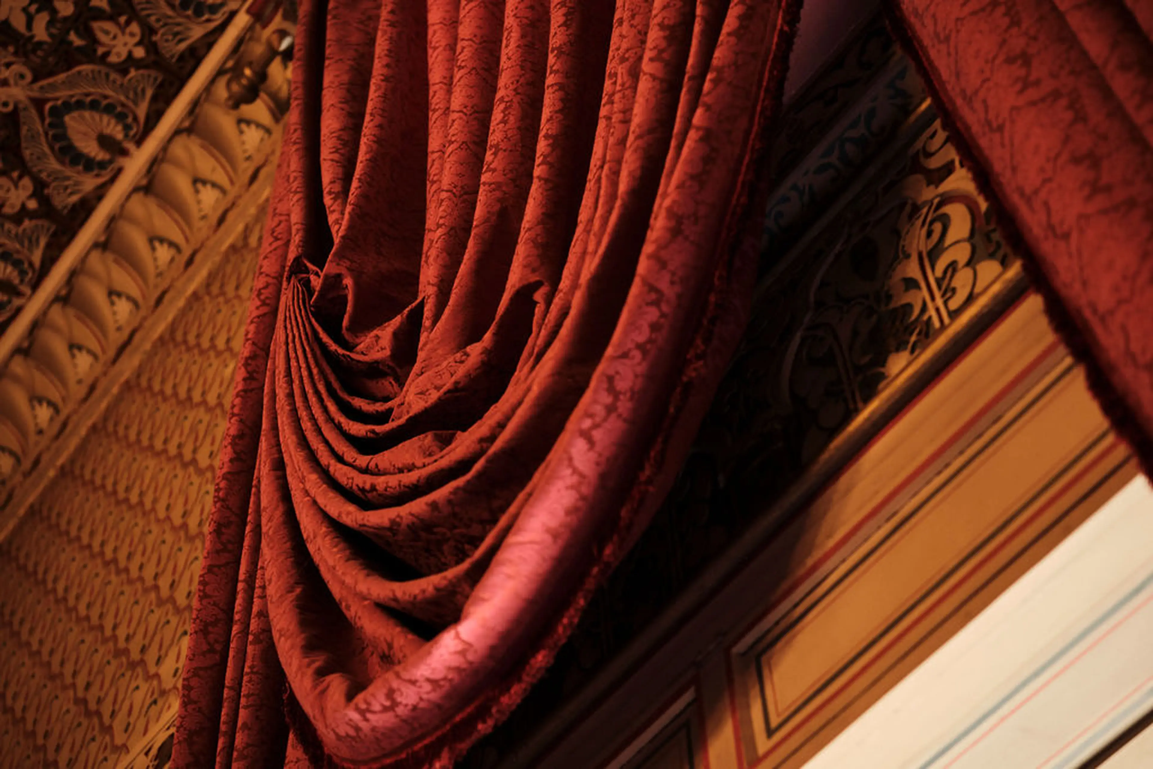 Roter Vorhang mit eleganten Drapierungen, umgeben von kunstvollen Verzierungen und goldenen Wanddetails.