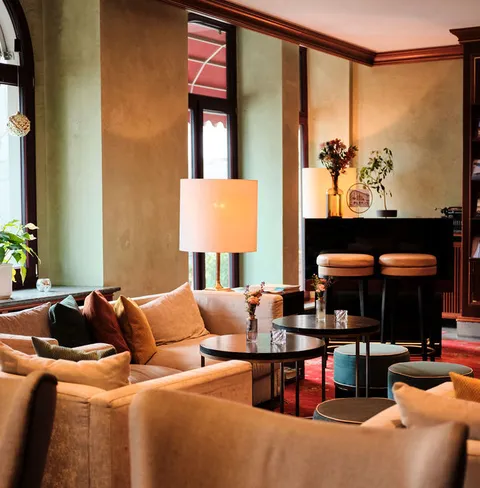 Gemütlicher Lounge-Bereich mit Sofas, Kissen, Stehlampen und einem Klavier im Hintergrund. Dezente Dekoration und warme Beleuchtung.