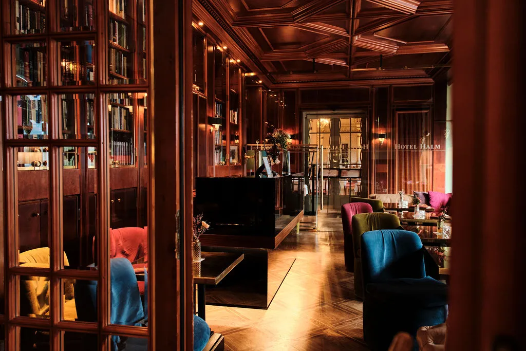 Elegantes Hotelzimmer mit Holzverkleidung, Bücherregalen und farbigen Polstersesseln, die eine gemütliche Atmosphäre schaffen.