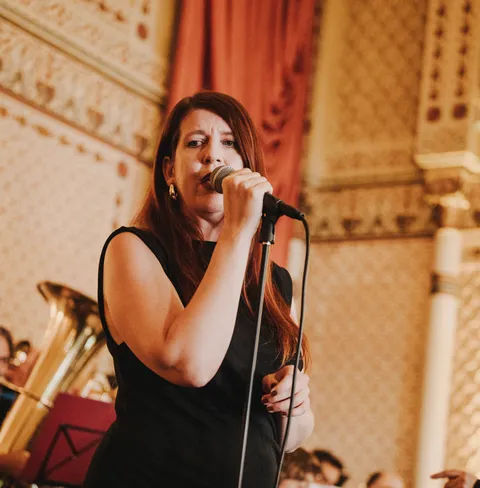 Eine Frau singt leidenschaftlich in ein Mikrofon, während sie vor der Big Band Konstanz in einem dekorativen Raum auftritt.