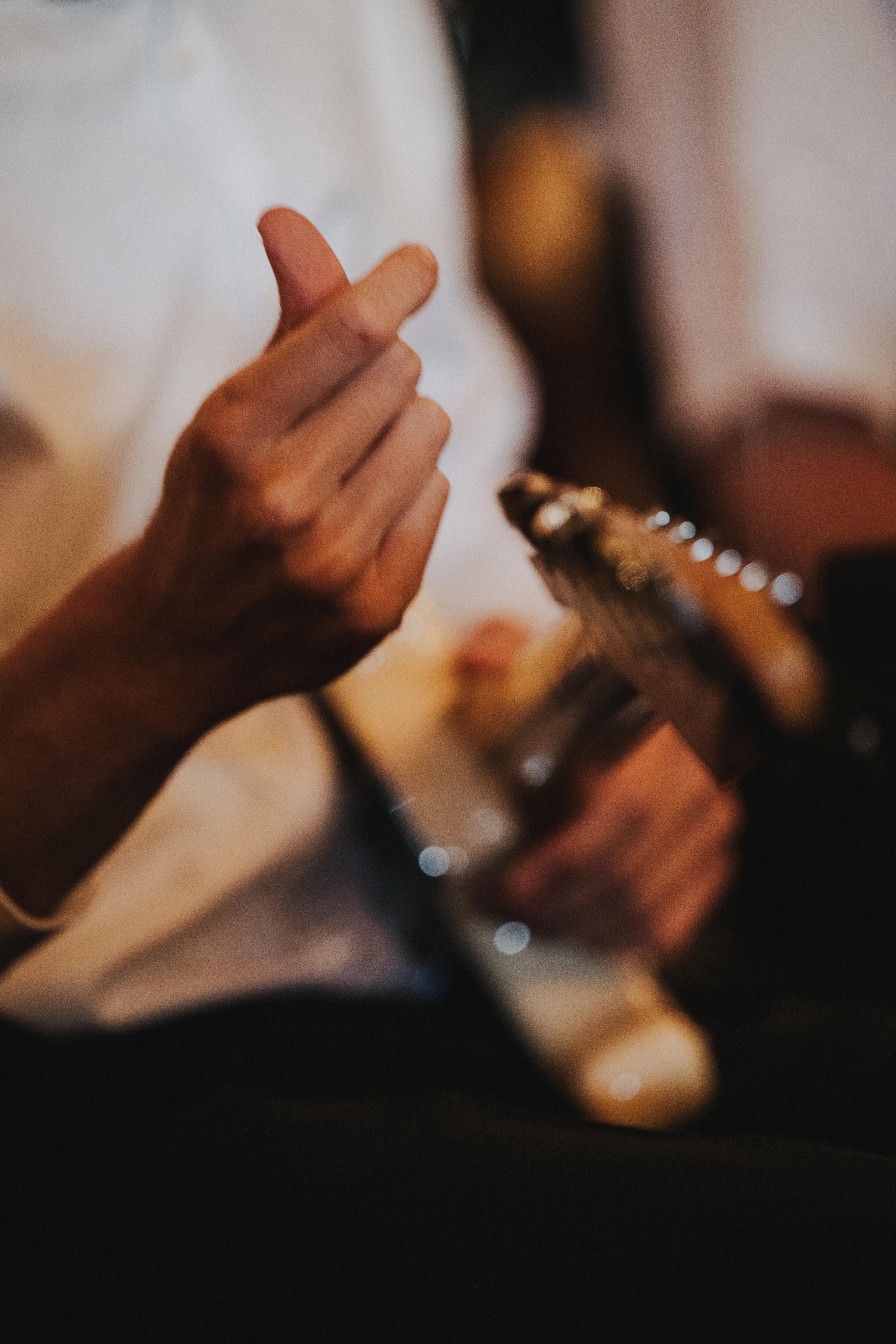 Ein Mann in weißem Hemd spielt eine E-Gitarre. Fokus liegt auf der Hand, die die Saiten zupft. Unscharfer Hintergrund.