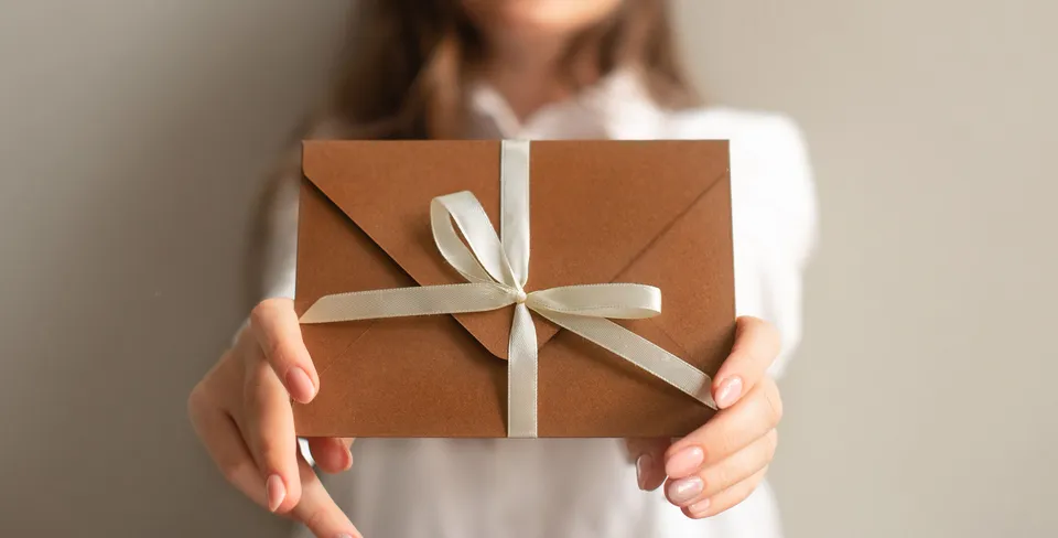 Geschenkgutschein mit Satinband wird in die Kamera gehalten