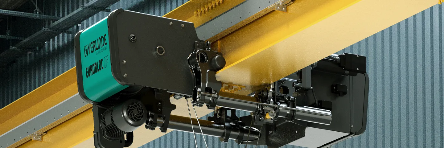 Industrial overhead crane with a motorized pulley system inside a large warehouse, featuring a yellow beam and a black and teal control unit.
