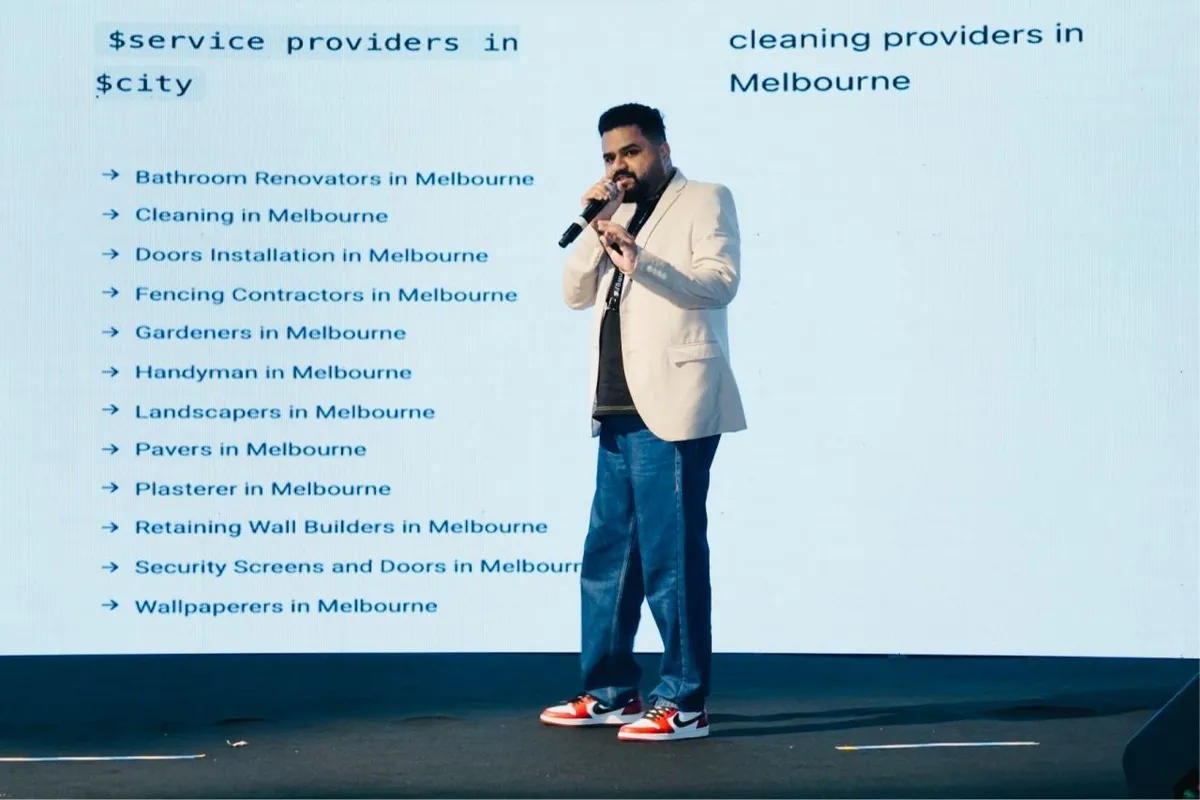 Devendra  presents on stage in front of a screen listing various service providers in Melbourne, including renovators and gardeners.