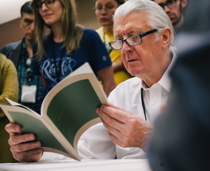 A photograph of Matthew Carter, a distinguished man with pulled back white hair and glasses reading a booklet