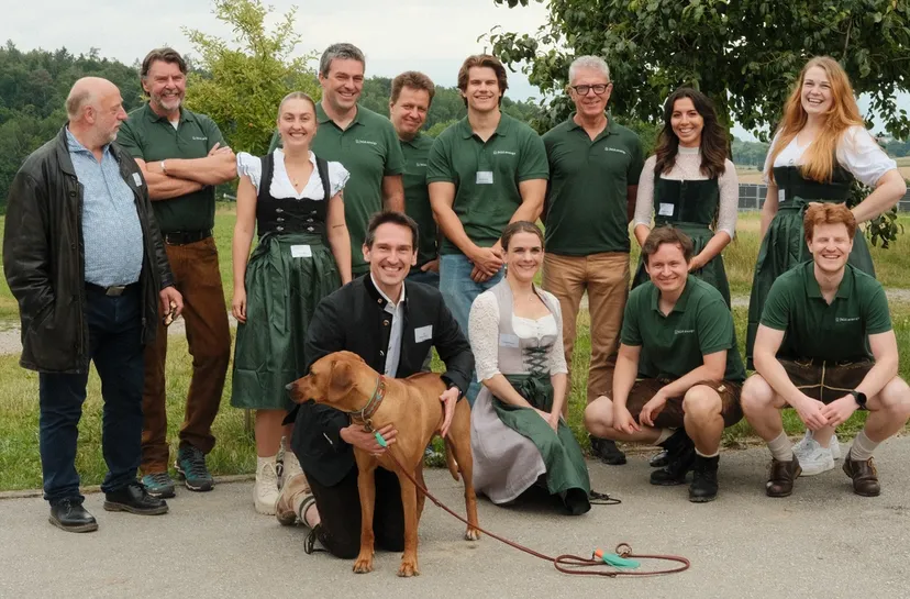 A group of people in traditional attire and green shirts, posing outdoors with a brown dog on a leash.