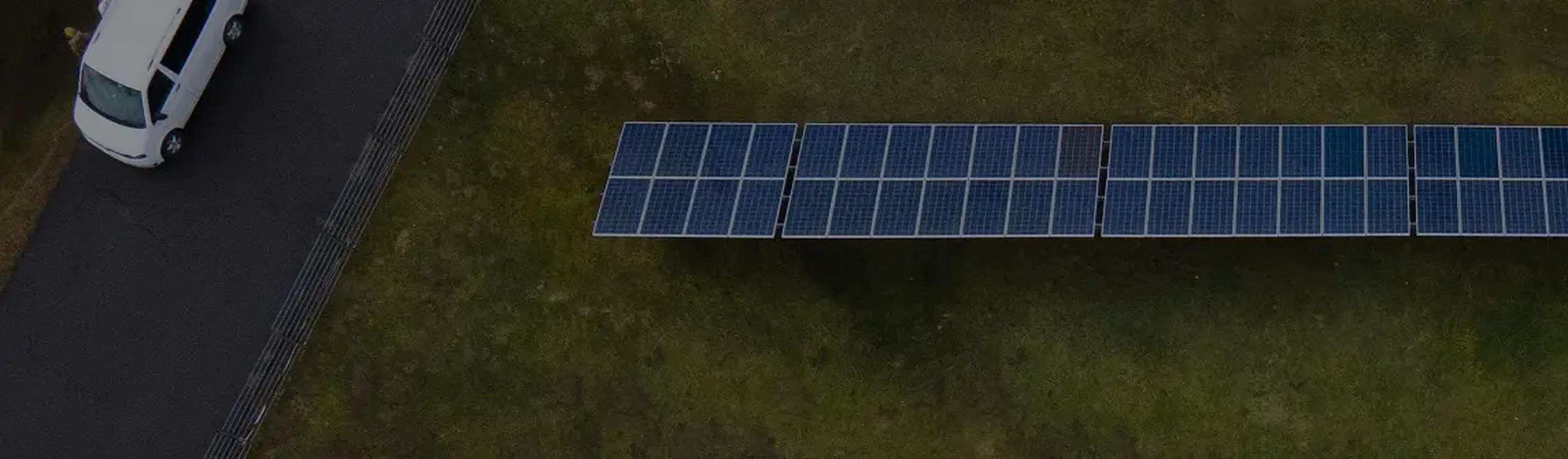 Aerial view of a solar panel array on grass near a road with a parked white van.