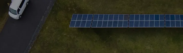 Aerial view of a solar panel array on grass near a road with a parked white van.