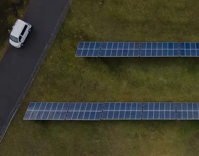 Aerial view of two rows of solar panels on grass near a road with a white van.