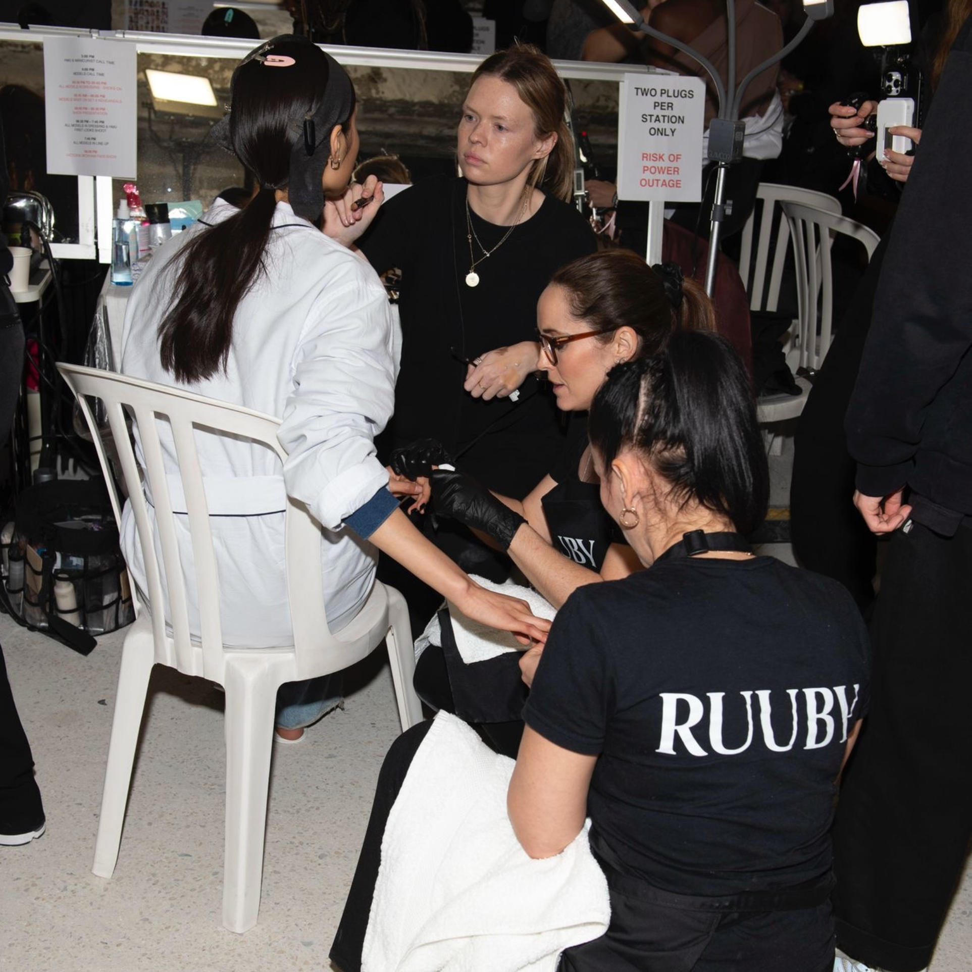 Ruuby manicurists in branded T-shirts preparing a model's nails backstage at a fashion show, working at a mirrored station