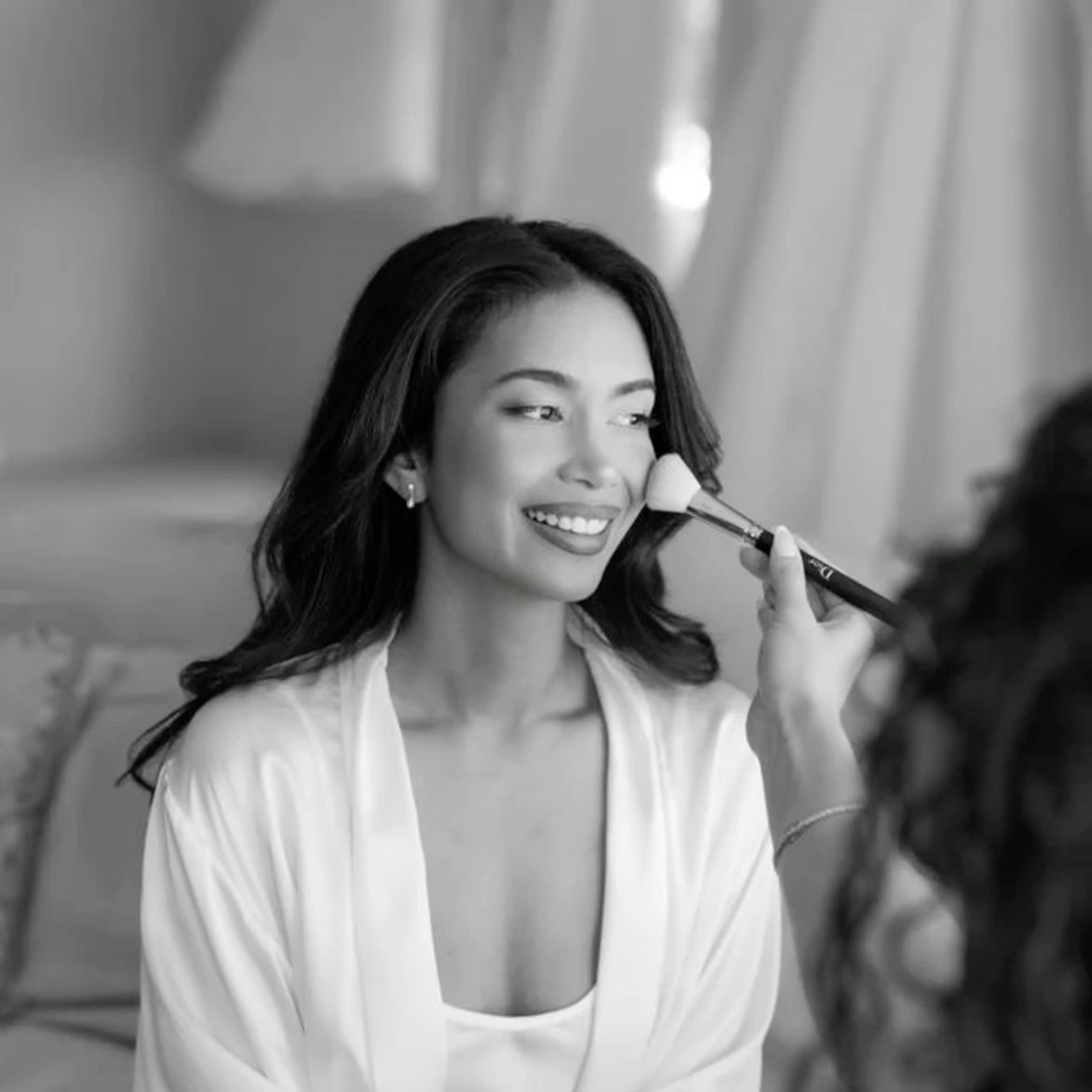 Smiling bride having bridal makeup applied with a brush while getting ready on her wedding day