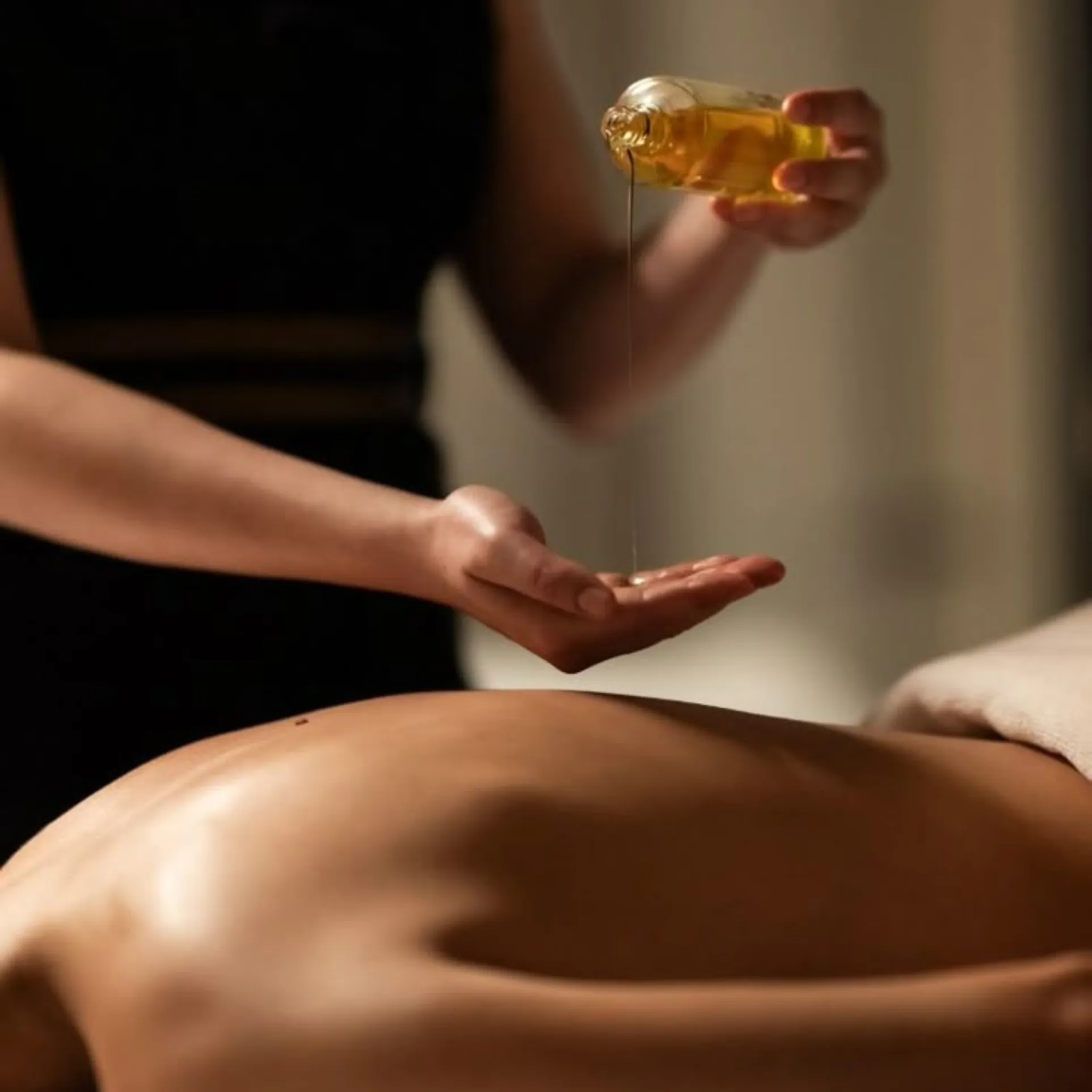 Therapist pouring aromatherapy oil before a massage during an at-home treatment