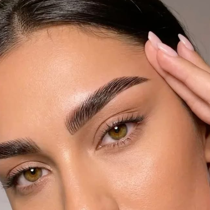 Close-up of a woman's face showing full, sculpted brows with the defined, hair-like strokes of a microblading treatment.