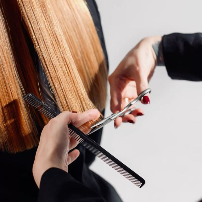 Ruuby hairdresser cutting long auburn hair with scissors and a comb during an at-home haircut