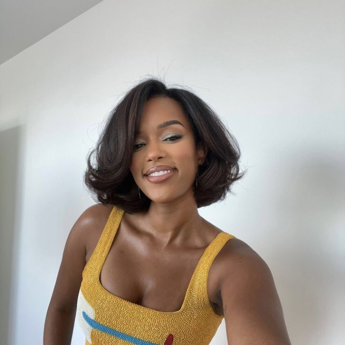 Woman with short, voluminous blow-dried dark hair with a soft curl, wearing a yellow embellished top.