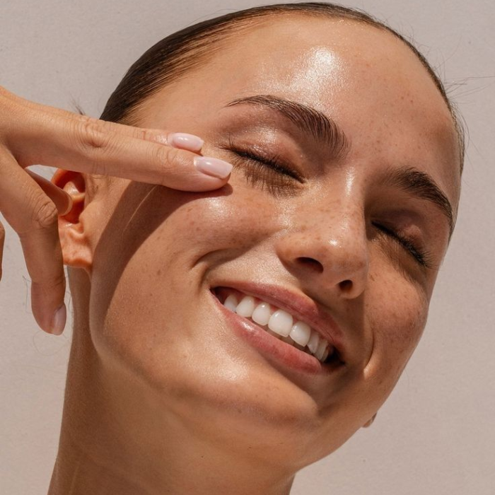 Close-up of a smiling woman with smooth, glowing skin and groomed brows, showing the results of facial waxing.