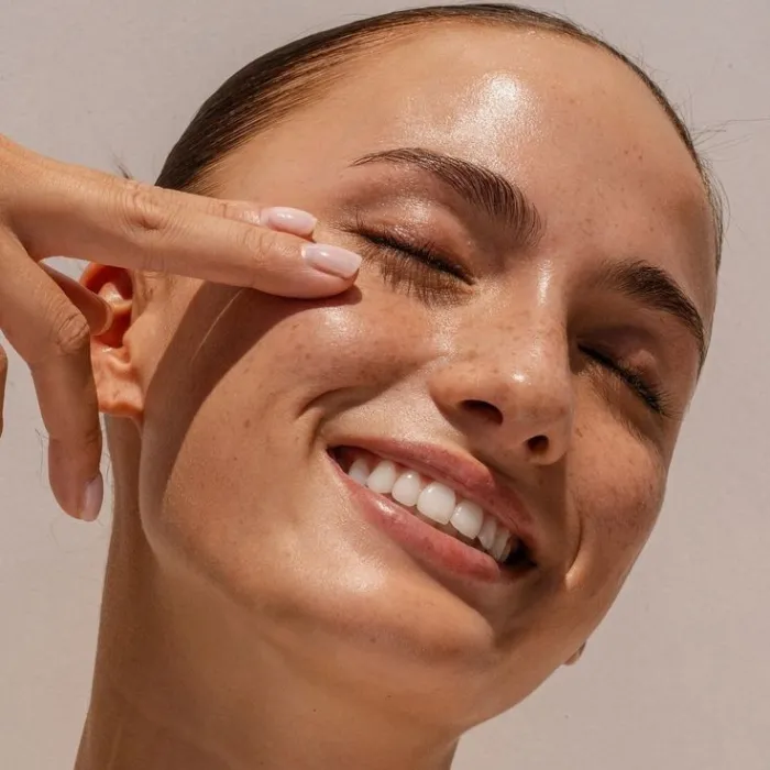 Close-up of a smiling woman with smooth, glowing skin and groomed brows, showing the results of profilo.