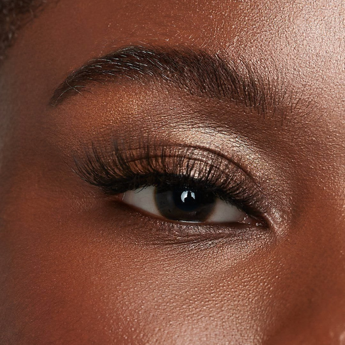 Close-up of a woman's eye showing full, voluminous lash extensions, with a defined brow and shimmering eyeshadow.