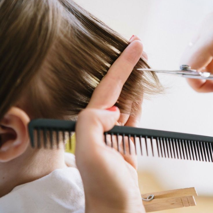Hairdresser trimming a young child's hair, using a comb and scissors on a fine section.