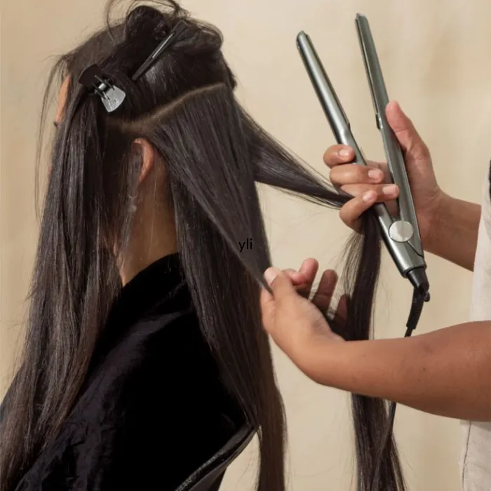 Stylist using flat-iron straighteners to dry-style a section of a client's long dark hair, with the top sections clipped up