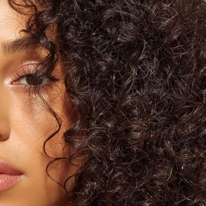 Close-up of a woman with defined natural curls framing her face, caught in soft light.
