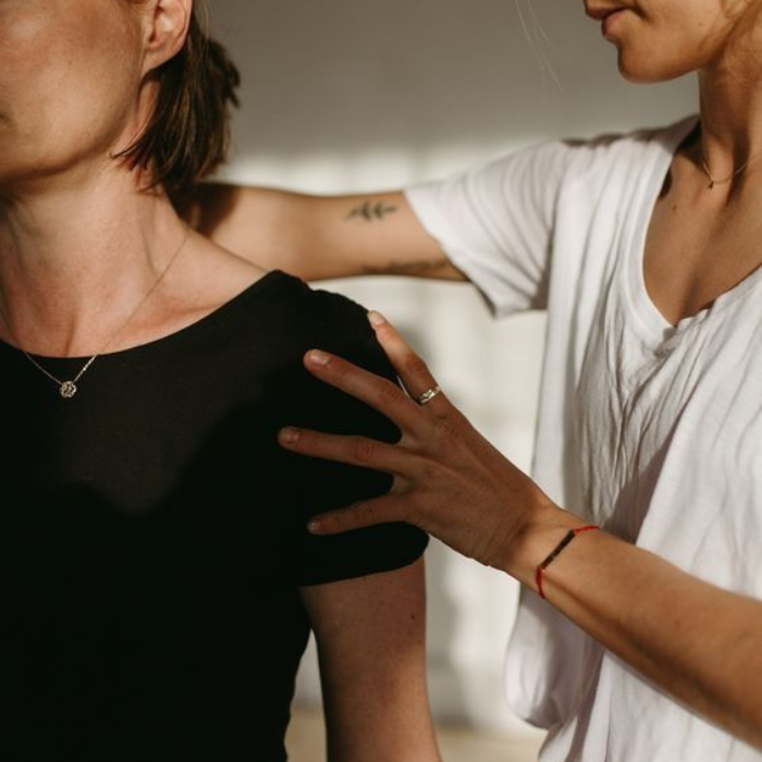 Clinician assessing a woman's shoulder and posture during a physiotherapy or osteopathy session.