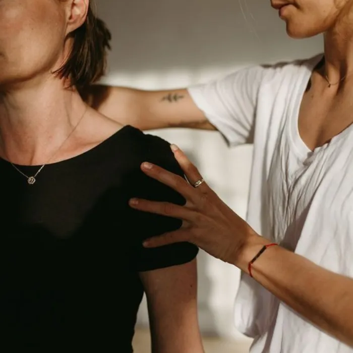 Clinician assessing a woman's shoulder and posture during a physiotherapy or osteopathy session.