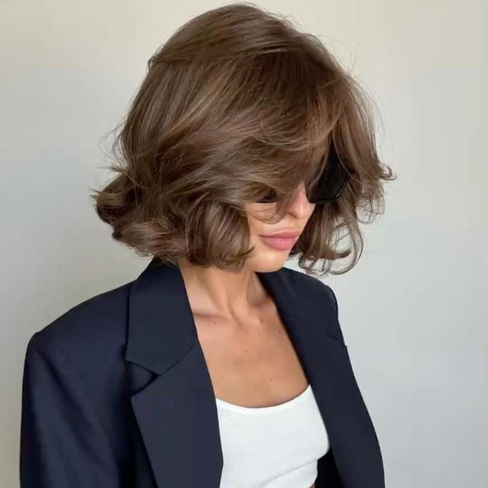 Woman with short, bouncy brown blow-dried hair wearing a white top and navy blazer.