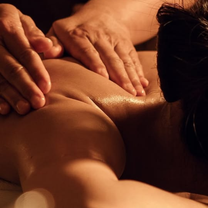 A therapist's hands performing a Swedish massage on a person's oiled back in warm, low lighting.