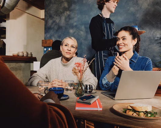 Two women behind a table with a laptop and a notebook on it