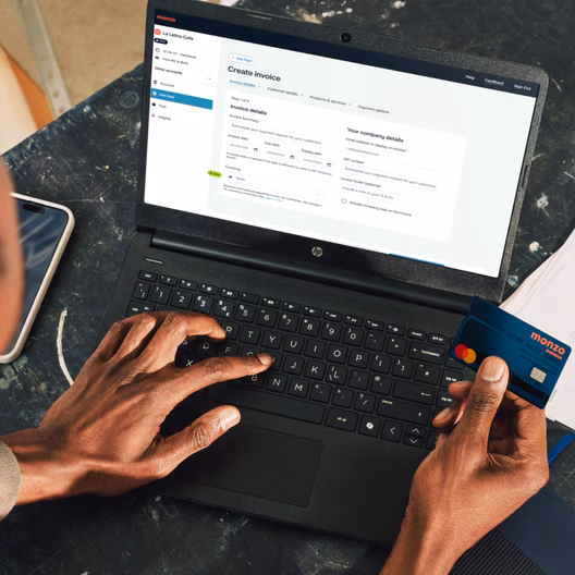 Someone creating an invoice in Monzo Business on a laptop while holding their business card.
