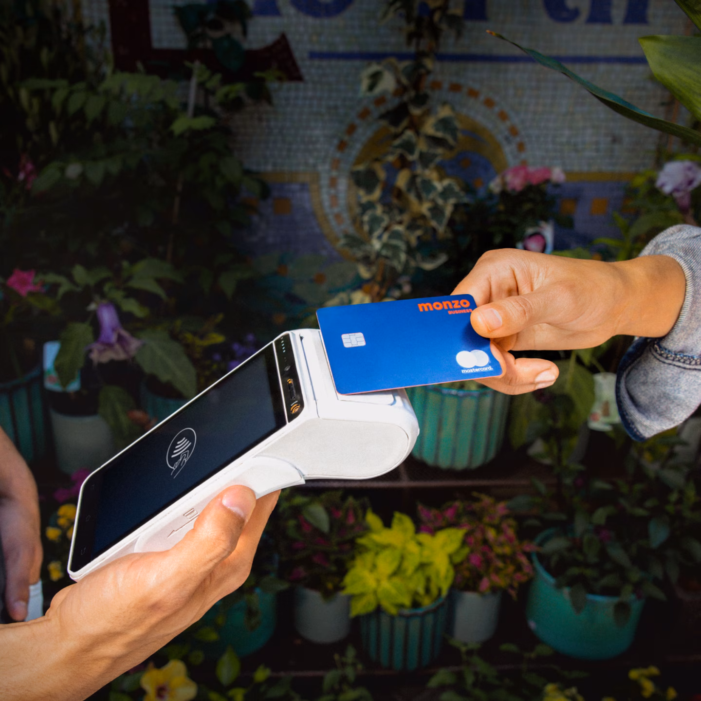 Persona sosteniendo una tarjeta Monzo y un lector de tarjetas al aire libre.