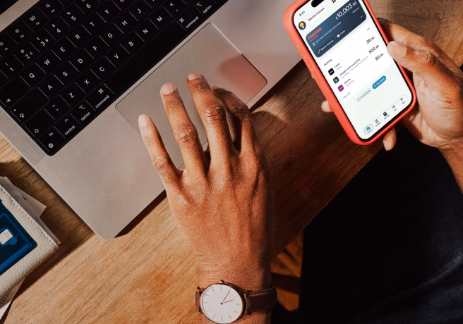 Phone displaying a Monzo Business account beside a laptop on a desk.