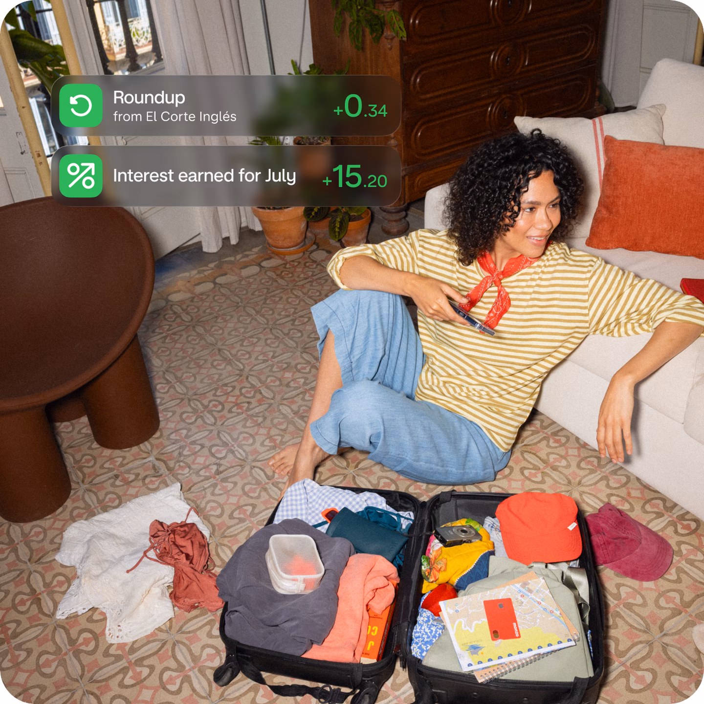 Person relaxing beside an open suitcase while round-up savings accumulate on screen.