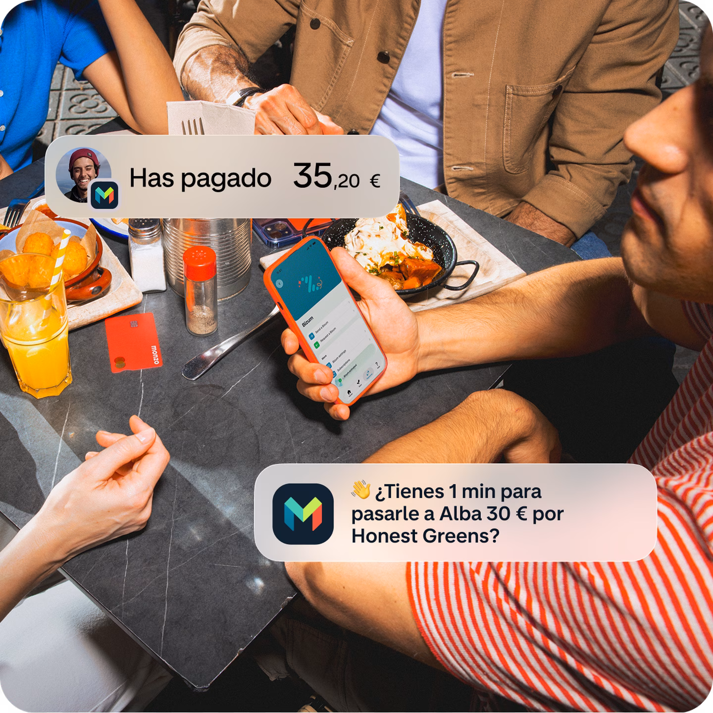 Imagen de un grupo de amigos compartiendo una comida en un restaurante, vista desde arriba. Una persona sostiene un móvil y aparecen notificaciones superpuestas de Monzo que muestran un pago de 35,20 € y un recordatorio para pagar 30 € a Alba por Honest Greens.